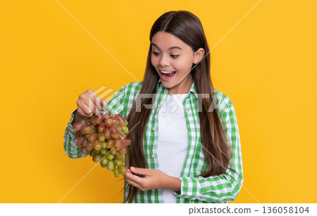 amazed child with ripe grapes bunch on yellow background 136058104