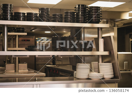A professional kitchen with dishes, pots, plates and kitchen utensils on the shelves. A professional kitchen with dishes, pots, plates and kitchen utensils on the shelves. 136058174