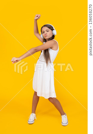 teen girl listen music in headphones and danc on yellow background 136058270