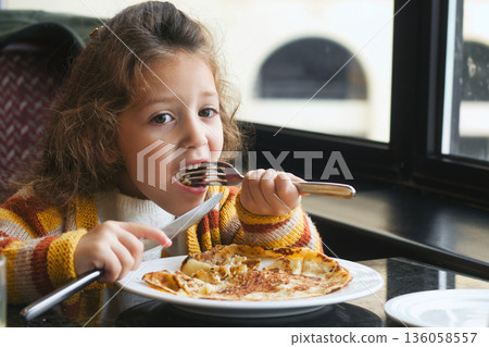 A young white Caucasian girl eating a breakfast pancake with a knife and fork A young white Caucasian girl eating a breakfast pancake with a knife and fork 136058557