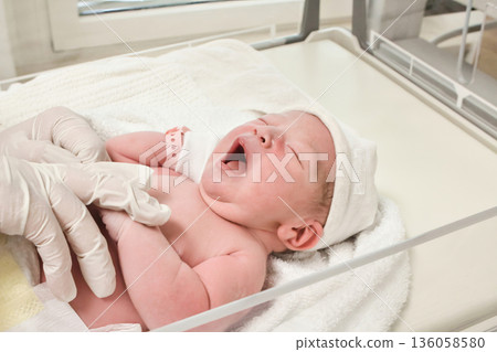 A newborn baby wearing a plastic identity bracelet being placed in a cot by a nurse in the delivery room at a maternity ward in hospital - concept of new life and motherhood 136058580