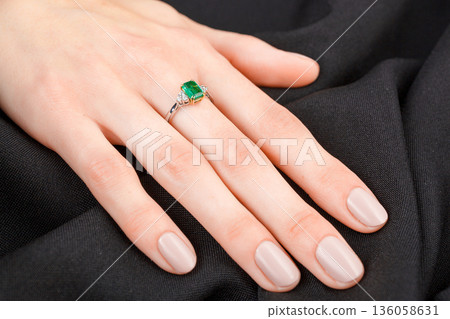 Beautiful female hand with gold ring with diamonds and emerald on gray background Beautiful female hand with gold ring with diamonds and emerald on gray background 136058631