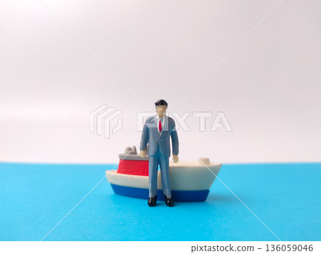 Miniature scale model figure of a man standing next to a small toy boat. Miniature scale model figure of a man standing next to a small toy boat. 136059046