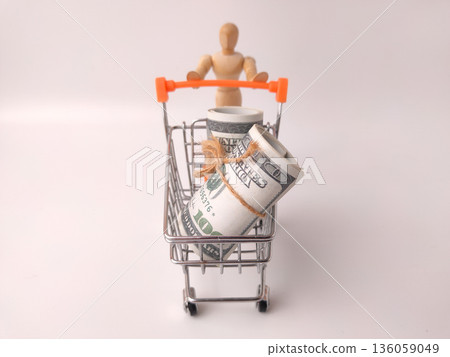 Shopping cart toy with a wooden artist's figure pushing it, and a roll of US currency inside. 136059049