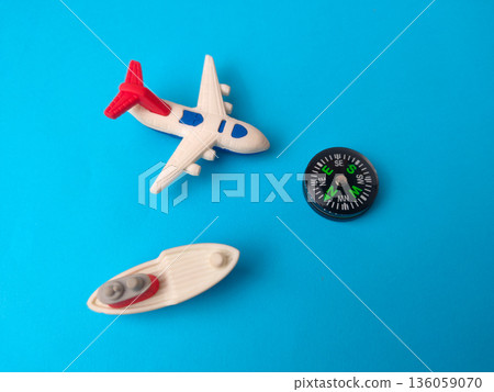 Small toy airplane, a toy boat, and a miniature compass on a blue background. Small toy airplane, a toy boat, and a miniature compass on a blue background. 136059070