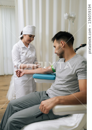 Nurse preparing arm for blood draw procedure, collecting test sample from male patient for medical diagnostic purposes in clinical laboratory setting. Concept of healthy lifestyle. 136059194