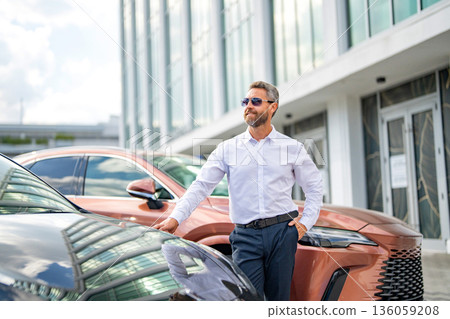 Dealership success. Rich man dealer near expensive car. Luxury dealership business. Confident rich businessman dealer. Mature businessman. Rich business man expressing success. Copy space Dealership success. Rich man dealer near expensive car. Luxury dealership business. Confident rich businessman dealer. Mature businessman. Rich business man expressing success. Copy space 136059208