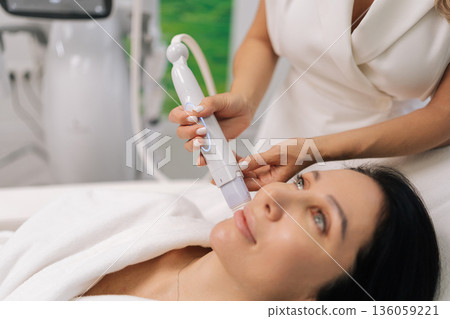 Closeup hands of cosmetologist using microneedle device to middle-aged woman face in beauty clinic, focusing on anti-aging and skin rejuvenation for healthy complexion. Concept of healthy lifestyle. Closeup hands of cosmetologist using microneedle device to middle-aged woman face in beauty clinic, focusing on anti-aging and skin rejuvenation for healthy complexion. Concept of healthy lifestyle. 136059221
