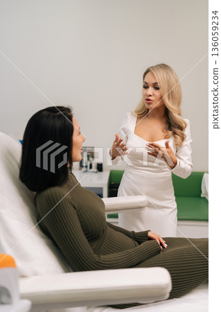 Portrait of blonde cosmetologist in white dress consulting female client about beauty treatments and skincare regimen, gesturing with hands in modern aesthetic clinic. Concept of beauty treatment. Portrait of blonde cosmetologist in white dress consulting female client about beauty treatments and skincare regimen, gesturing with hands in modern aesthetic clinic. Concept of beauty treatment. 136059234
