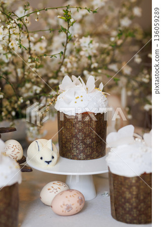 Easter cake on stand with painted eggs and bunny treat, spring blossom background, soft light 136059289