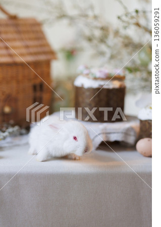 White bunny on Easter table with cakes, eggs and spring blossoms, soft light White bunny on Easter table with cakes, eggs and spring blossoms, soft light 136059291
