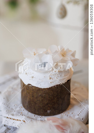 Easter cake with white icing and flower topper on lace cloth, soft minimal background Easter cake with white icing and flower topper on lace cloth, soft minimal background 136059308