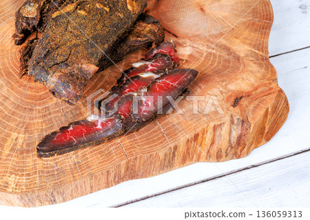 Cured beef meat sits on wooden board with some slices placed beside it food preparation. Cured beef meat sits on wooden board with some slices placed beside it food preparation. 136059313