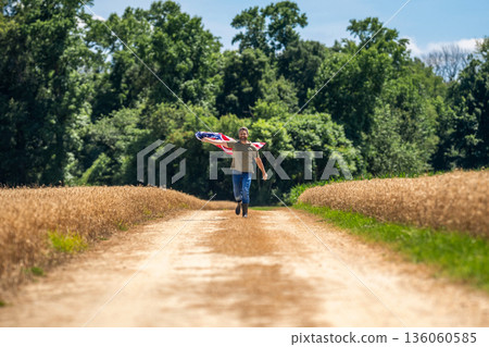Flag of USA. Independence day. Man in field. Man with American flag in crop field. Independence day of America. 4th of July. American labor day. American flag and man farmer. Country life Flag of USA. Independence day. Man in field. Man with American flag in crop field. Independence day of America. 4th of July. American labor day. American flag and man farmer. Country life 136060585