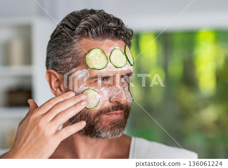 Facial mask of cucumber. Cosmetic beauty man with cucumber slices on face. Hispanic man with facial mask. Man fill skin with vitamin. Man applying facial mask with cucumber. Cooling face treatment Facial mask of cucumber. Cosmetic beauty man with cucumber slices on face. Hispanic man with facial mask. Man fill skin with vitamin. Man applying facial mask with cucumber. Cooling face treatment 136061224