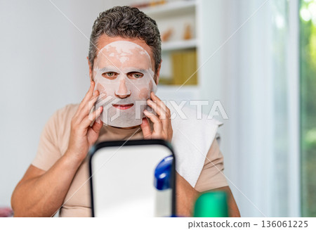 Hispanic male use moisturizing facial beauty mask. Collagen for glowing skin. Man with cloth moisturizing mask on face. Rejuvenating fabric mask. Face skincare hydrating sheet collagen, copy space 136061225