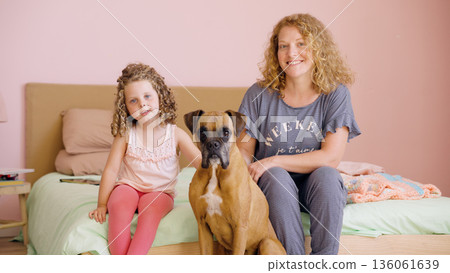Mother daughter and boxer dog posing in bedroom Mother daughter and boxer dog posing in bedroom 136061639