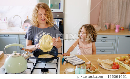 Mother and daughter cooking pancakes in kitchen Mother and daughter cooking pancakes in kitchen 136061661
