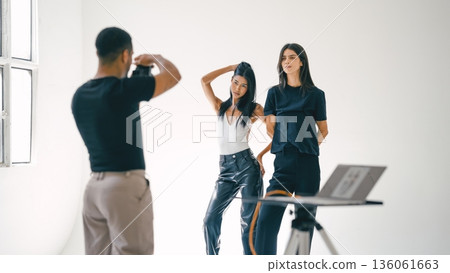 Photographer taking photos of two fashion models in studio Photographer taking photos of two fashion models in studio 136061663