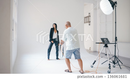 Photographer taking pictures of model posing in photo studio 136061681