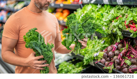 Man shopping kale cabbage in grocery store. Healthy lifestyle. Fresh food store. Man in grocery store. Man shopping in vegetable supermarket. Grocery consumer with kale cabbage. Raw kale cabbage Man shopping kale cabbage in grocery store. Healthy lifestyle. Fresh food store. Man in grocery store. Man shopping in vegetable supermarket. Grocery consumer with kale cabbage. Raw kale cabbage 136061728