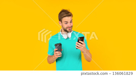 amazed man hold smartphone and coffee cup on yellow background, communication 136061829