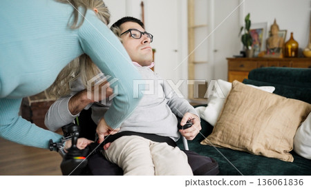 Caregiver assisting man buckling into power wheelchair 136061836