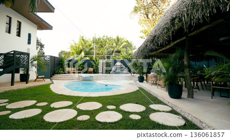 Resort swimming pool with tropical garden and thatched roof patio 136061857