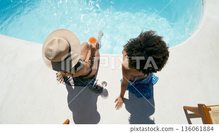 Women friends relaxing by swimming pool with drinks Women friends relaxing by swimming pool with drinks 136061884