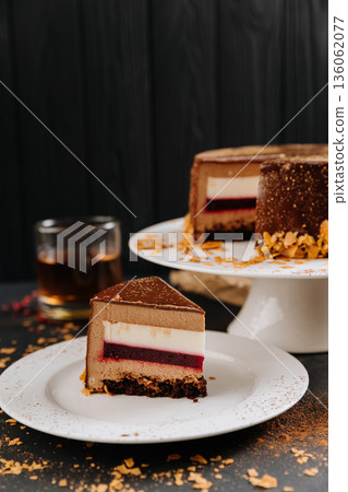 Chocolate mousse cake slice with berry layer on plate, cocoa dust, dark backdrop Chocolate mousse cake slice with berry layer on plate, cocoa dust, dark backdrop 136062077