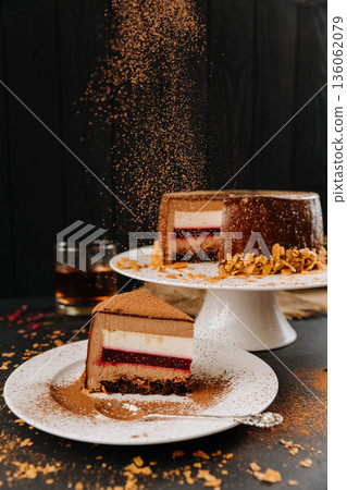Layered chocolate mousse cake slice with berry layer and falling cocoa dust Layered chocolate mousse cake slice with berry layer and falling cocoa dust 136062079