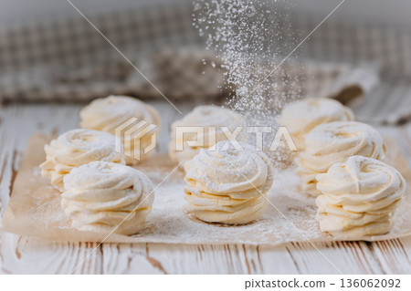Powdered sugar falling on vanilla zephyr rosettes on parchment, rustic background 136062092