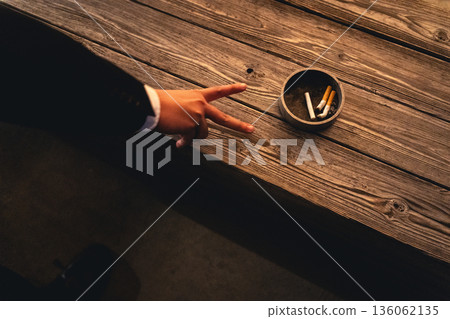 A hand making a peace sign towards an ashtray on a wooden bench at night A hand making a peace sign towards an ashtray on a wooden bench at night 136062135