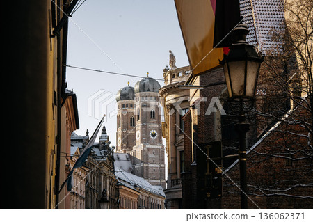 Historic Munich Old Town Street With Cathedral Of Our Dear Lady: Narrow Urban Alley Framing Iconic Twin Domed Church Towers And Traditional Bavarian Architecture Historic Munich Old Town Street With Cathedral Of Our Dear Lady: Narrow Urban Alley Framing Iconic Twin Domed Church Towers And Traditional Bavarian Architecture 136062371