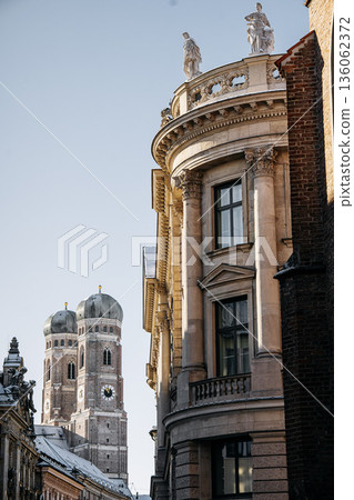 Historic Munich Old Town Street With Cathedral Of Our Dear Lady: Narrow Urban Alley Framing Iconic Twin Domed Church Towers And Traditional Bavarian Architecture Historic Munich Old Town Street With Cathedral Of Our Dear Lady: Narrow Urban Alley Framing Iconic Twin Domed Church Towers And Traditional Bavarian Architecture 136062372