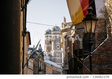 Historic Munich Old Town Street With Cathedral Of Our Dear Lady: Narrow Urban Alley Framing Iconic Twin Domed Church Towers And Traditional Bavarian Architecture Historic Munich Old Town Street With Cathedral Of Our Dear Lady: Narrow Urban Alley Framing Iconic Twin Domed Church Towers And Traditional Bavarian Architecture 136062376