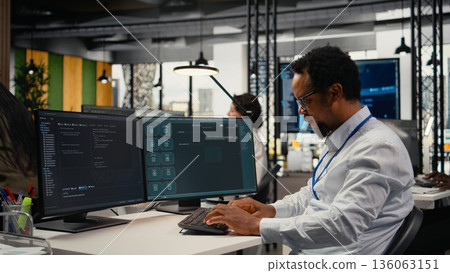 Programmer in office using AI LLM chatbot to get help optimizing systems performance metrics. IT worker in tech agency utilizing generative AI LLM assistant for faster software development, camera A 136063151