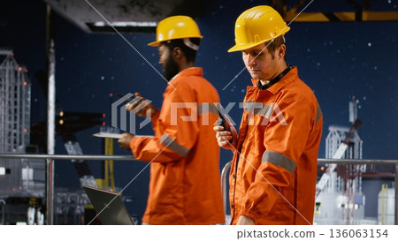 Male worker on drilling rig using walkie talkie to communicate across offshore platform, coordinating the colleagues for oil and gas extraction within the oil industry. Maritime pollution. Male worker on drilling rig using walkie talkie to communicate across offshore platform, coordinating the colleagues for oil and gas extraction within the oil industry. Maritime pollution. 136063154