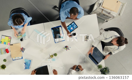 Top down view of surgeons staff in a clinic discussing therapy options and research analysis. The meeting highlights professionalism and innovation in healthcare planning. 136063157