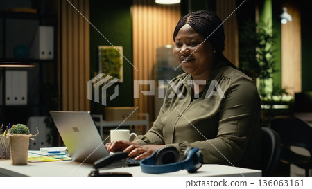 Portrait of black worker engaged in drafting updates and creating summary after hours. Organizing monthly planner, ensuring business goals and agenda items to meet enterprise targets. Camera B. 136063161