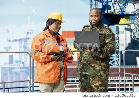 Military marine unit guarding offshore platform, supervising deck operations, ensuring compliance with safety protocols. Army soldier protecting worker doing preventative maintenance on drilling rig Military marine unit guarding offshore platform, supervising deck operations, ensuring compliance with safety protocols. Army soldier protecting worker doing preventative maintenance on drilling rig 136063315