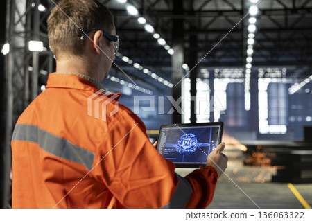 Technician controls automation machinery guided by AI and machine learning, managing industrial equipment within a busy industry plant to support logistic operation and manufacture. 136063322