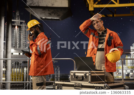 Agitated oil rig inspection officer evaluates fuel production systems and sweating, working in tension to ensure petroleum compliance and natural fuel extraction. Concerned engineer. 136063335