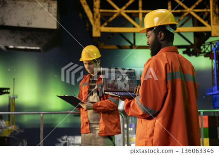 Environmental officer uses laptop on offshore rig under the northern lights, ensuring petroleum and fuel extraction on the platform. Compliance with oil and gas production industry. Environmental officer uses laptop on offshore rig under the northern lights, ensuring petroleum and fuel extraction on the platform. Compliance with oil and gas production industry. 136063346