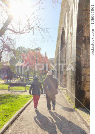 Old people walking along path beside historic aqueduct in sunny city park backlit sun and long shadows leisure scene travel lifestyle concept. High quality photo Old people walking along path beside historic aqueduct in sunny city park backlit sun and long shadows leisure scene travel lifestyle concept. High quality photo 136065061