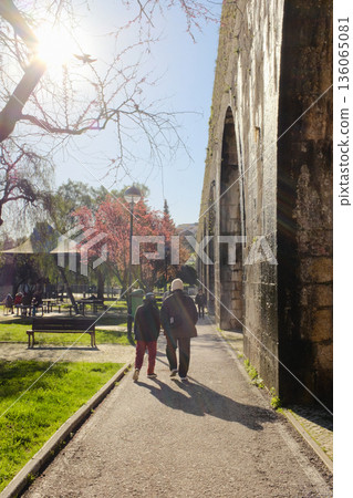Old people walking along path beside historic aqueduct in sunny city park backlit sun and long shadows leisure scene travel lifestyle concept. High quality photo Old people walking along path beside historic aqueduct in sunny city park backlit sun and long shadows leisure scene travel lifestyle concept. High quality photo 136065081