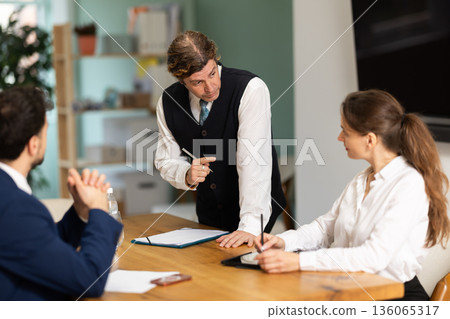 Working atmosphere, business colleagues gathering at table, and man participant stands up Working atmosphere, business colleagues gathering at table, and man participant stands up 136065317