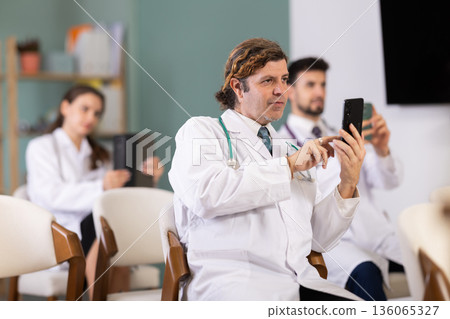 Medical students or doctors using mobile phones to scan QR-code during interactive lesson Medical students or doctors using mobile phones to scan QR-code during interactive lesson 136065327