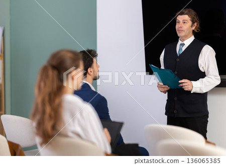 Male lecturer with folder addressed to attendees lecture Male lecturer with folder addressed to attendees lecture 136065385