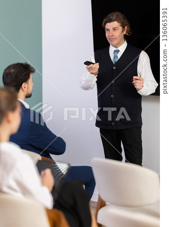 Male lecturer communicates and addressed to attendees, controls projector using remote control Male lecturer communicates and addressed to attendees, controls projector using remote control 136065391